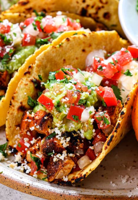 up close of chicken street tacos showing what they're made of: corn tortilla, chopped chicken, guacamole, pico de gallo and cotija cheese