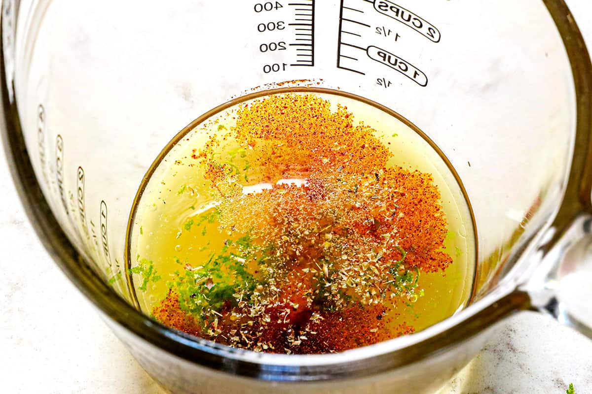 showing how to make cucumber salad by whisking vinegar, lime juice, olive oil and spices together in a measuring cup