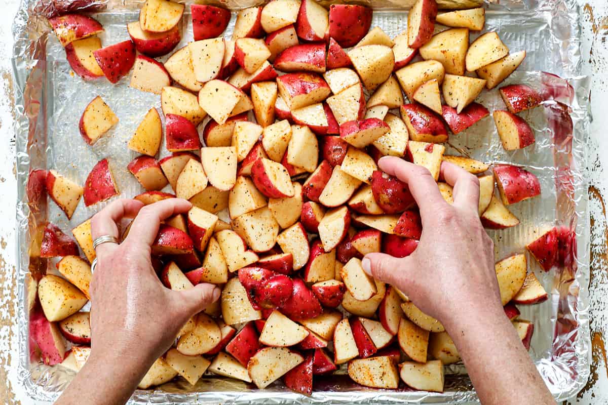 showing how to make red potato salad by tossing red skinned potatoes with olive oil and seasonings