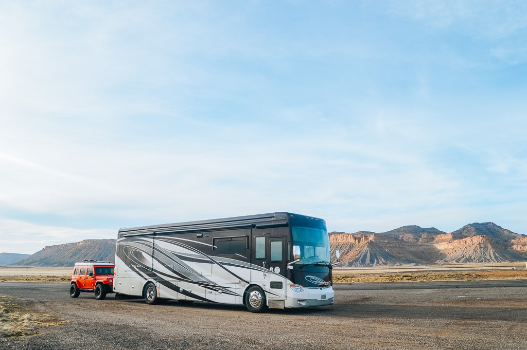 how to get paid as a Campground worker (workamper, campground host, etc.) - picture of a Class A RV towing a red Jeep