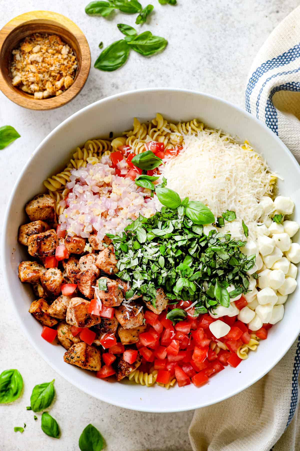 showing chicken pasta salad ingredients in a bowl: pasta, chicken, tomatoes, basil, onions, garlic, parmesan and mozzarella