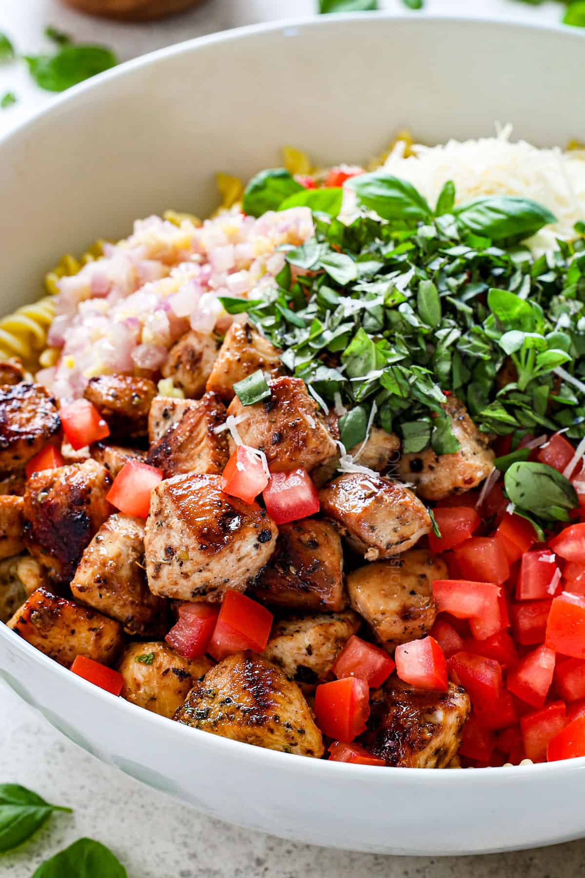 making chicken pasta salad in a large bowl with cooked chicken, tomatoes and basil