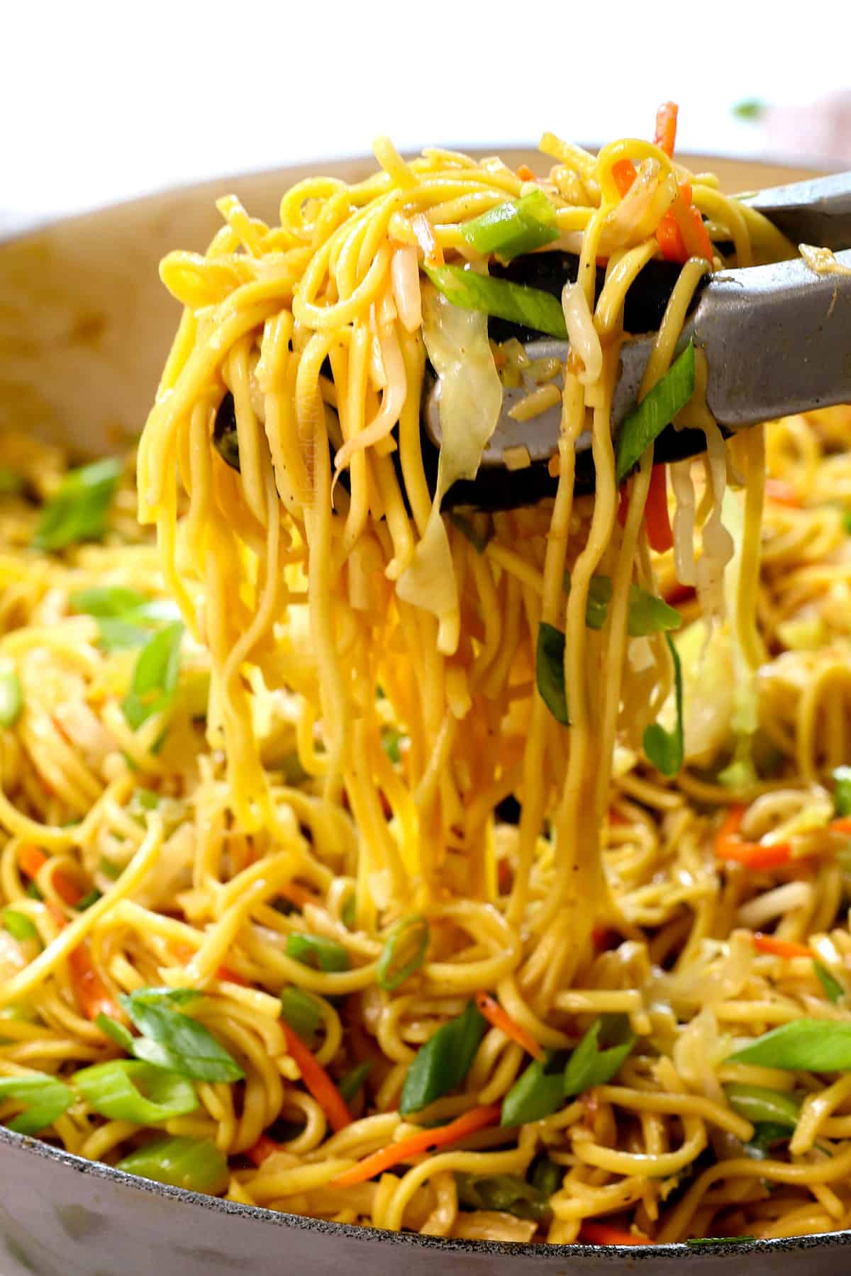 up close of scooping up chow mien with tongs showing their crispy, chewy texture