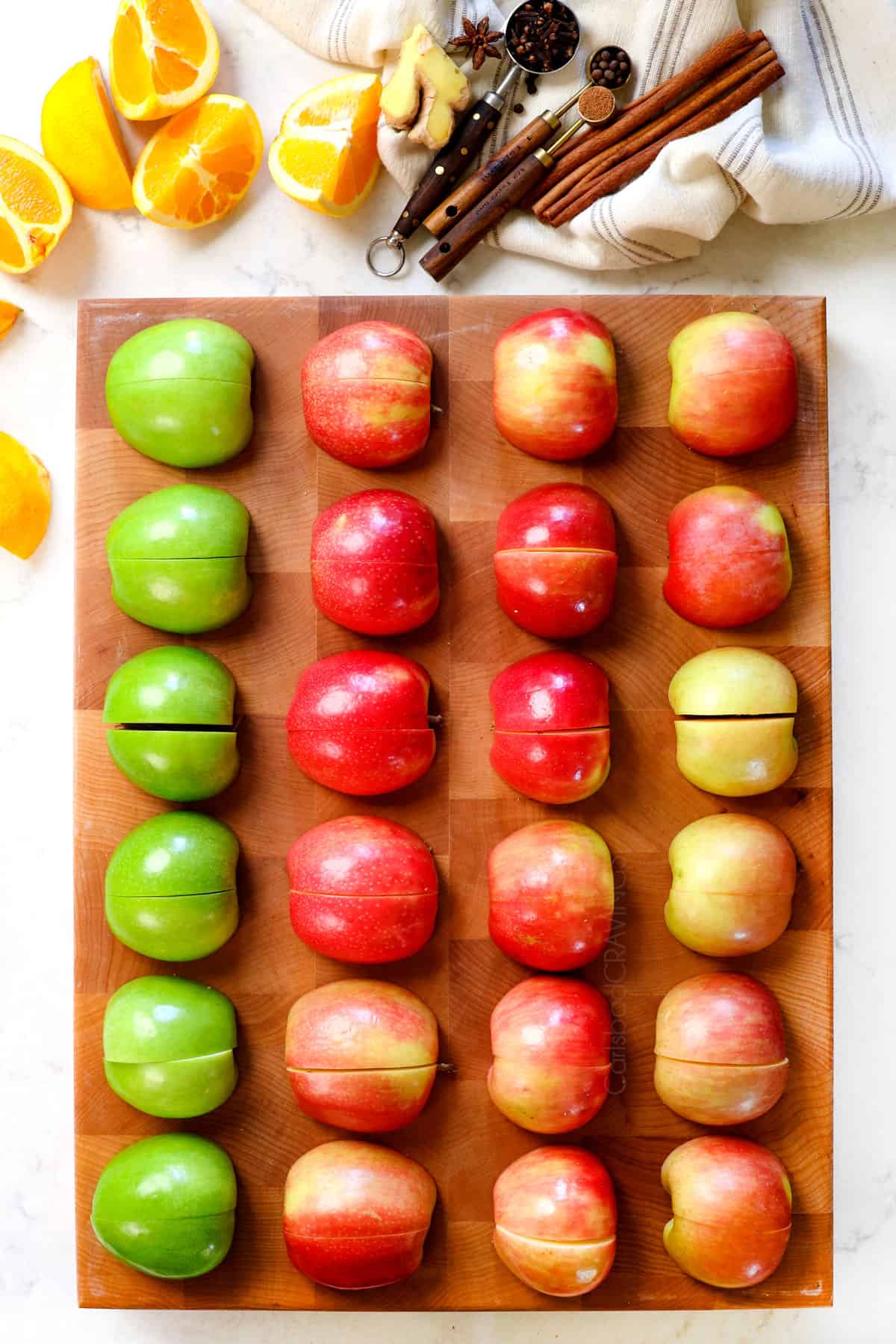 top view showing ingredients for apple cider recipe: apples, oranges, cinnamon, cloves, ginger and spices