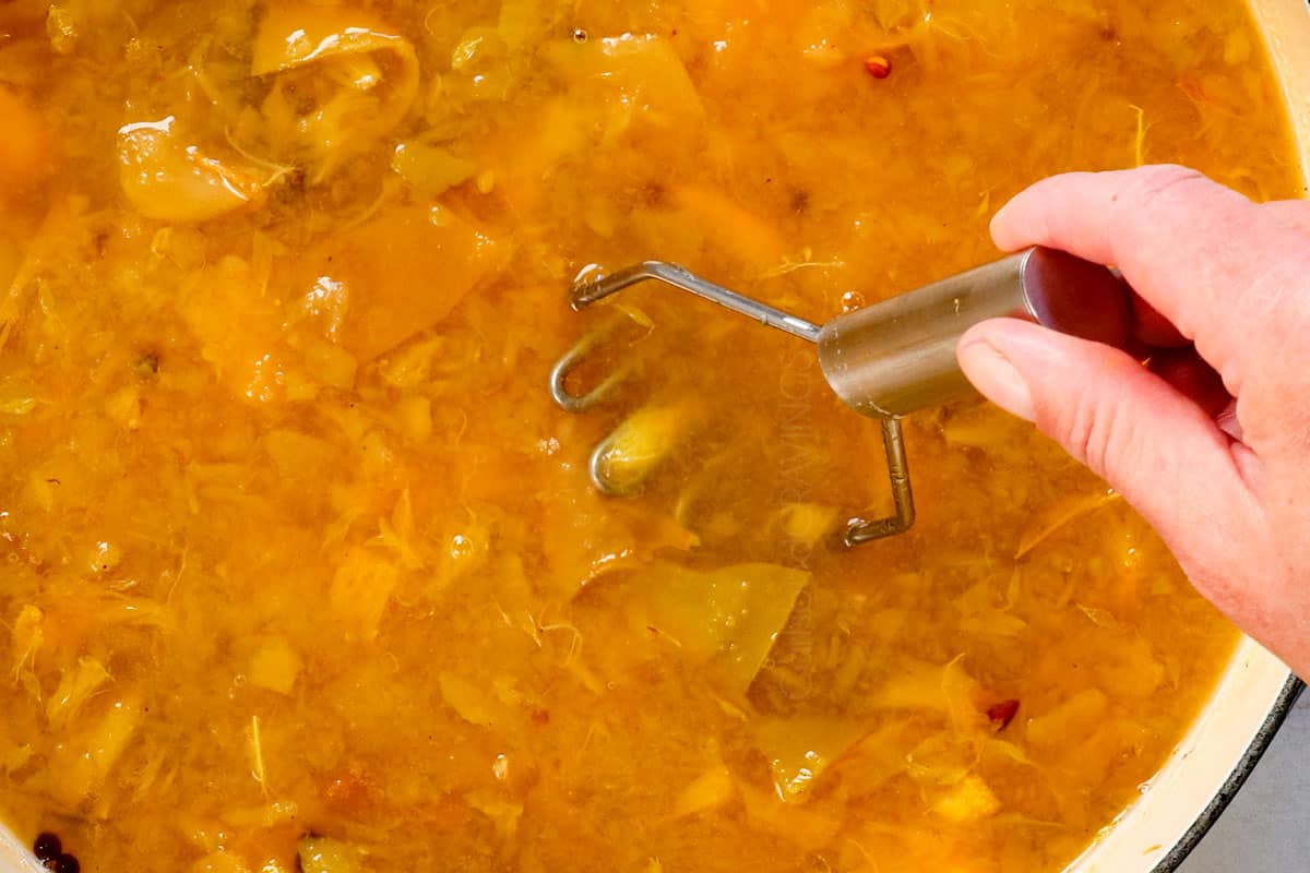 showing how to make apple cider recipe by mashing apples in the pot