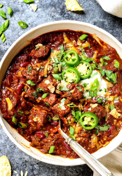 showing how to serve chili con carne (beef chili) by adding sour cream, green onions, jalapenos and chips