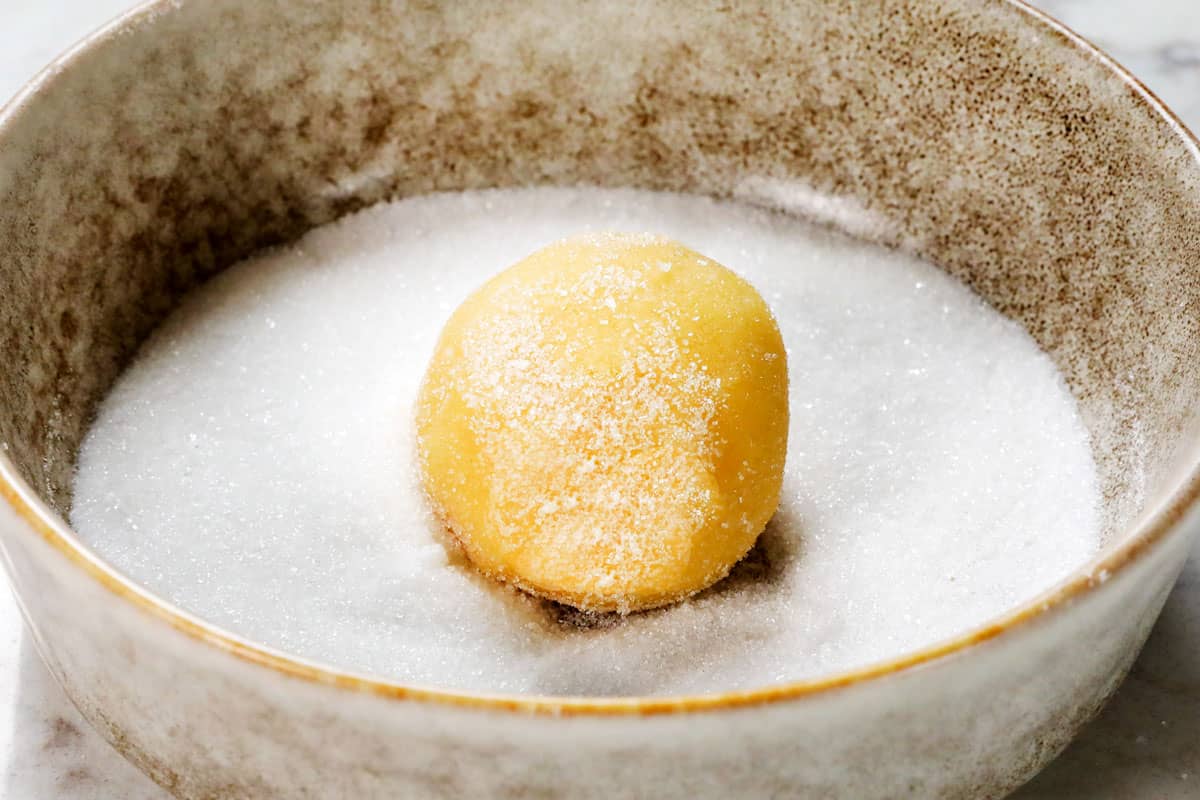 showing how to make sugar cookies by rolling the dough balls in sugar before baking