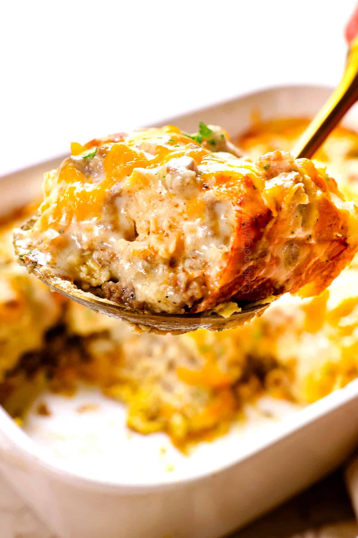 a slice of sausage gravy casserole on a serving spoon garnished with parsley