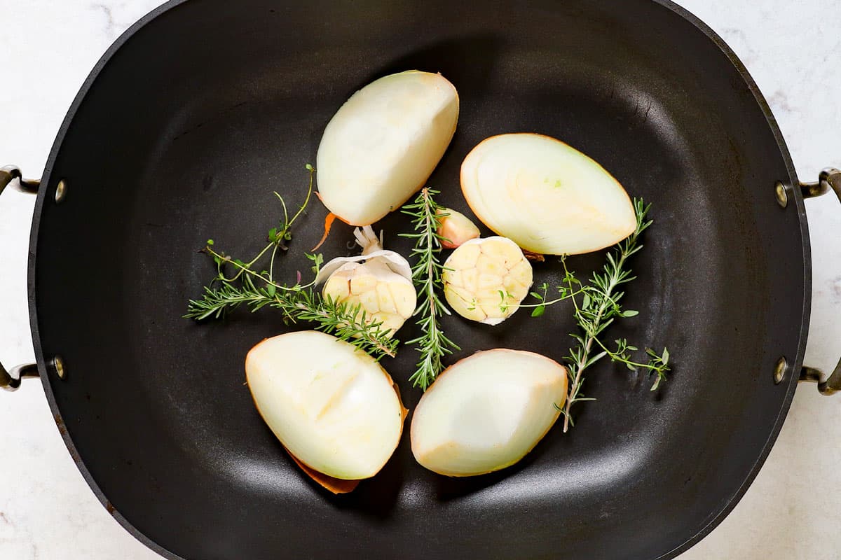 showing how to cook prime rib by adding onions, garlic, rosemary and thyme to a roasting pan