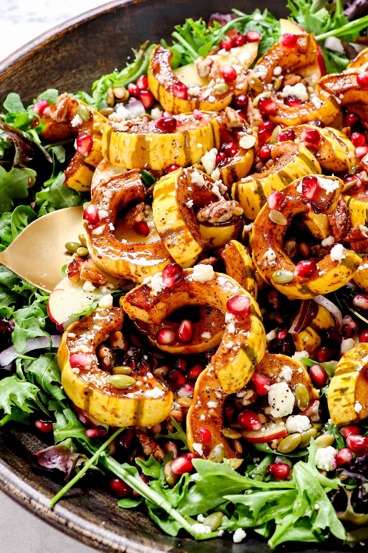 showing how to make squash salad by layering lettuce with red onions, apples, squash, feta, pepitas, and feta