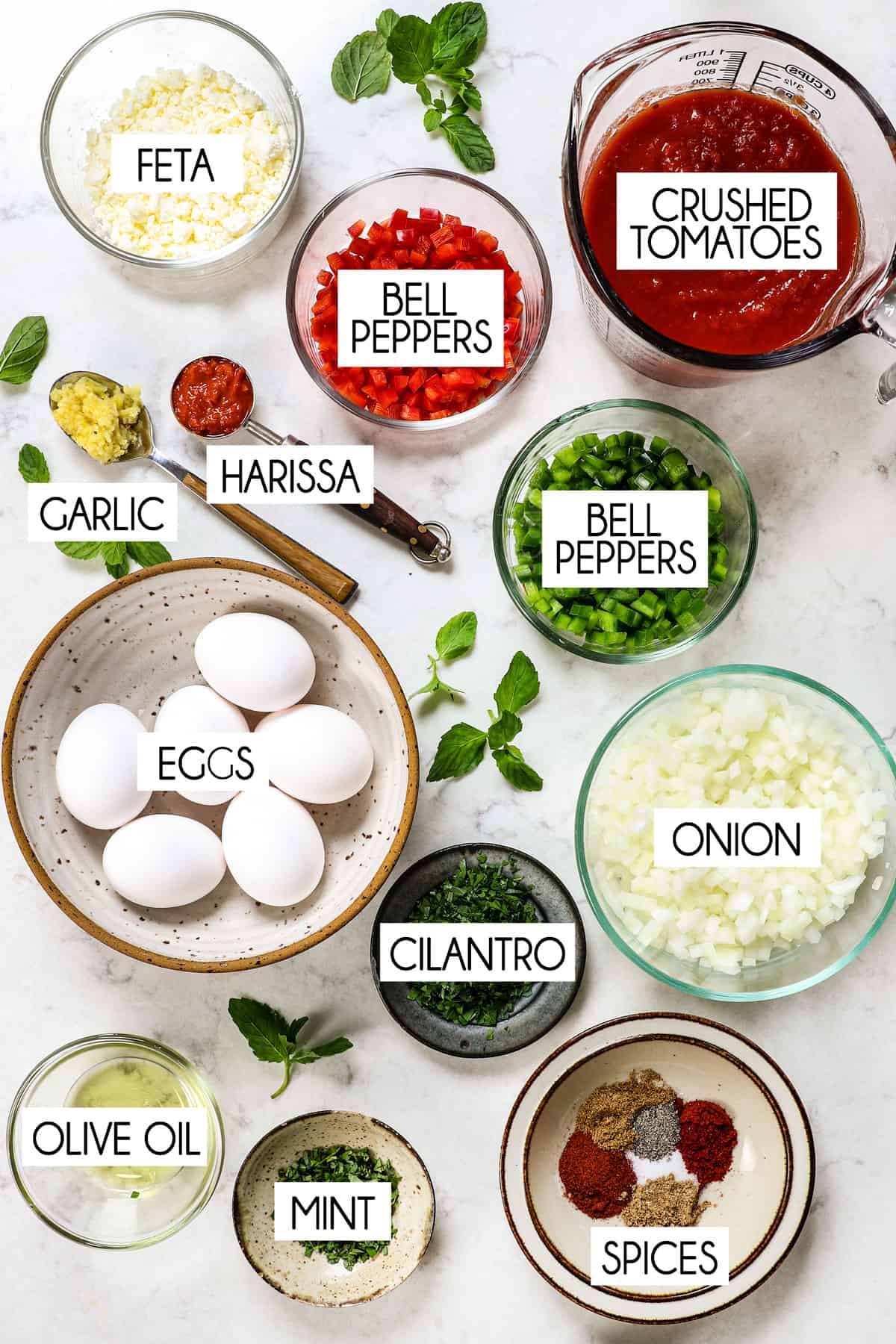top view showing ingredients for shakshuka recipe: crushed tomatoes, onions, bell peppers, garlic, onions, cilantro, olive oil, feta and spices