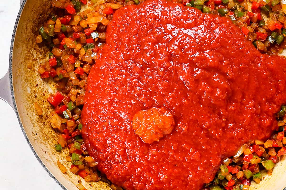 showing how to make shakshuka by adding crushed tomatoes and harissa
