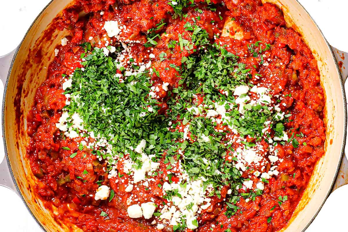 showing how to make shakshuka by stirring in feta, cilantro and parsley