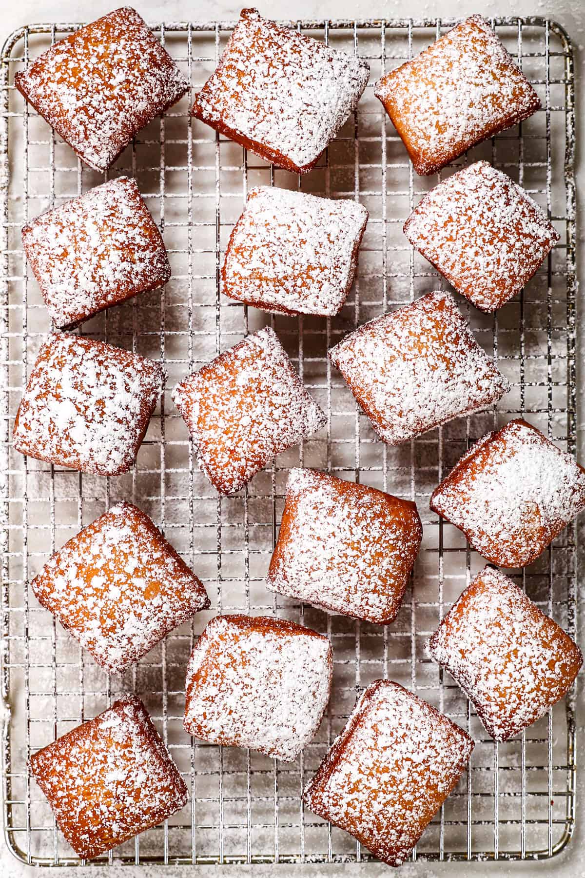 showing how to make beignets recipe with a top view of covering with powdered sugar