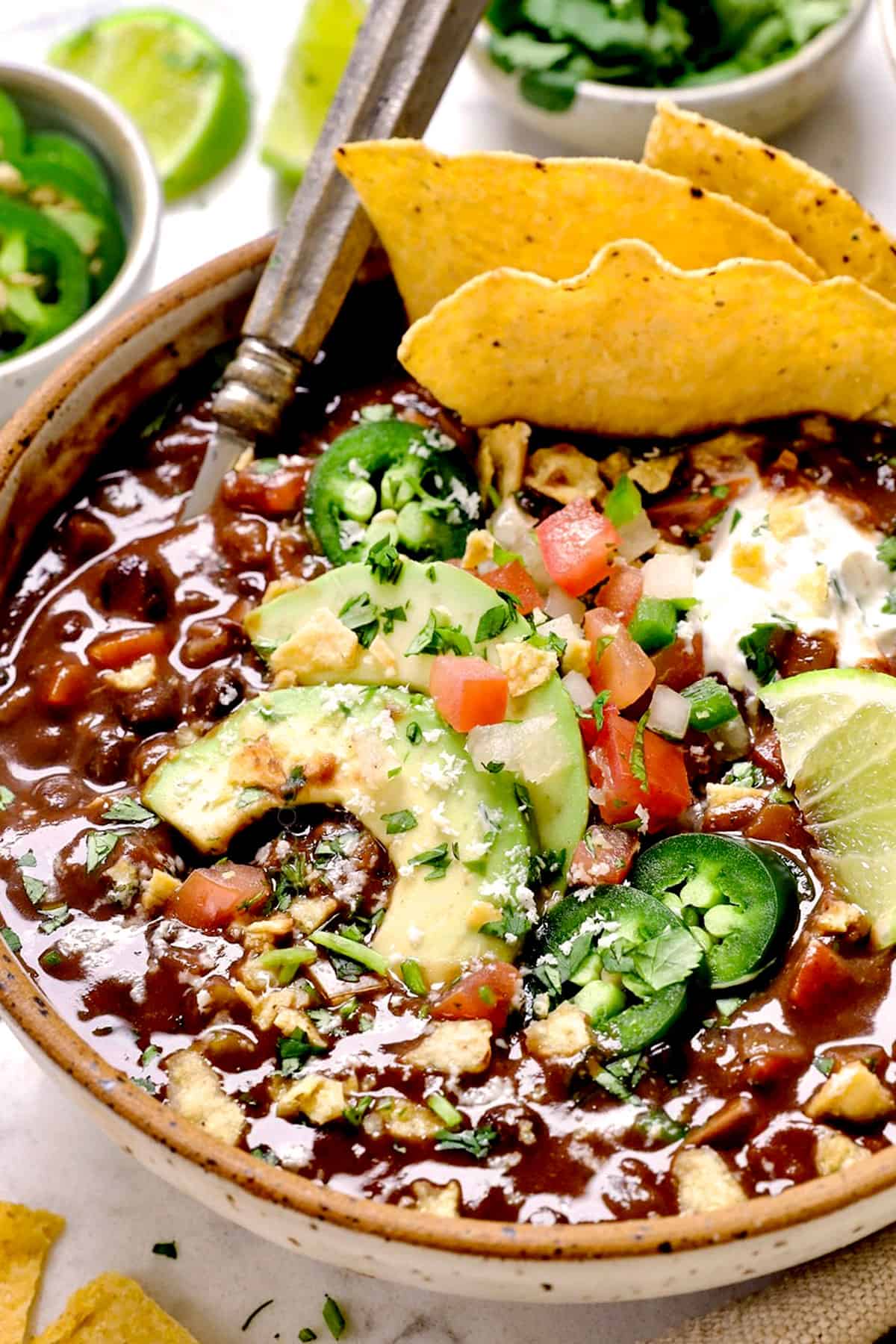 showing how to serve black bean soup recipe with chips, avocado, tomatoes, jalapeno and limes