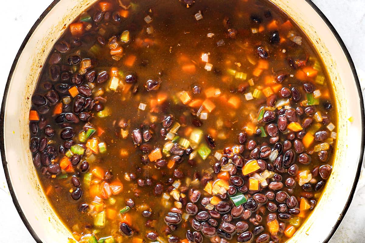 showing how to make black bean soup by adding beans and vegetable broth and simmering soup