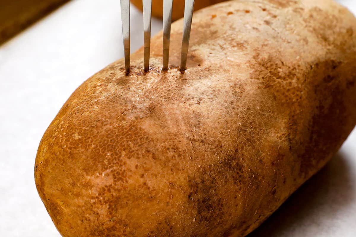showing how to make a baked potato in the oven by piercing it with a fork