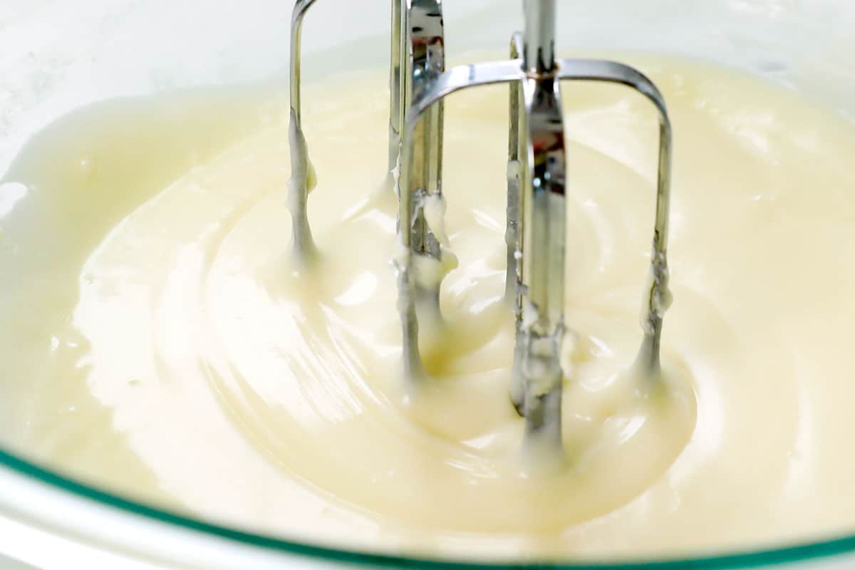 showing how to make lemon poppy seed cake recipe by whisking the cream cheese, powdered sugar and lemon juice together