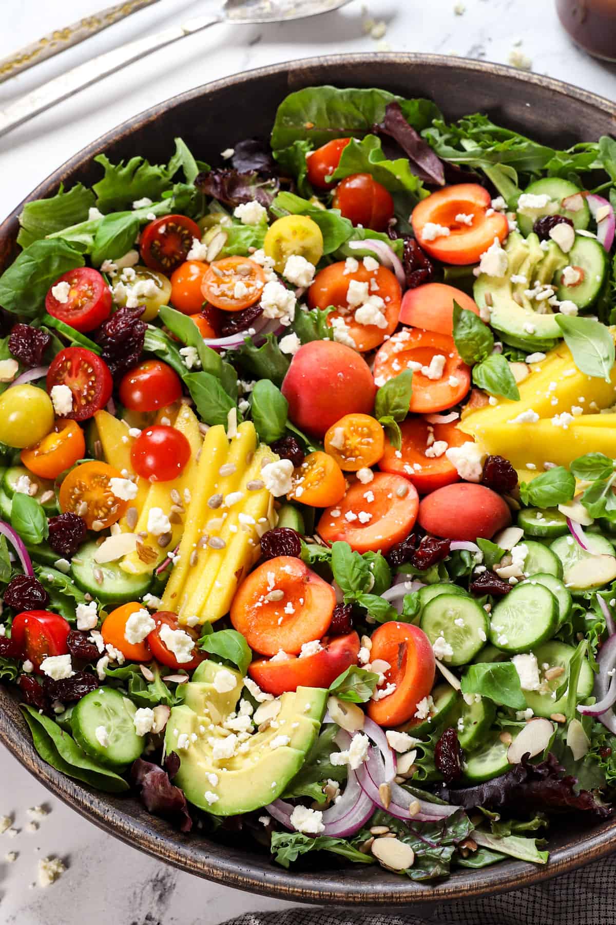 showing how to make cherry salad by adding the spring mix, cherries, mangos, tomatoes to a bowl