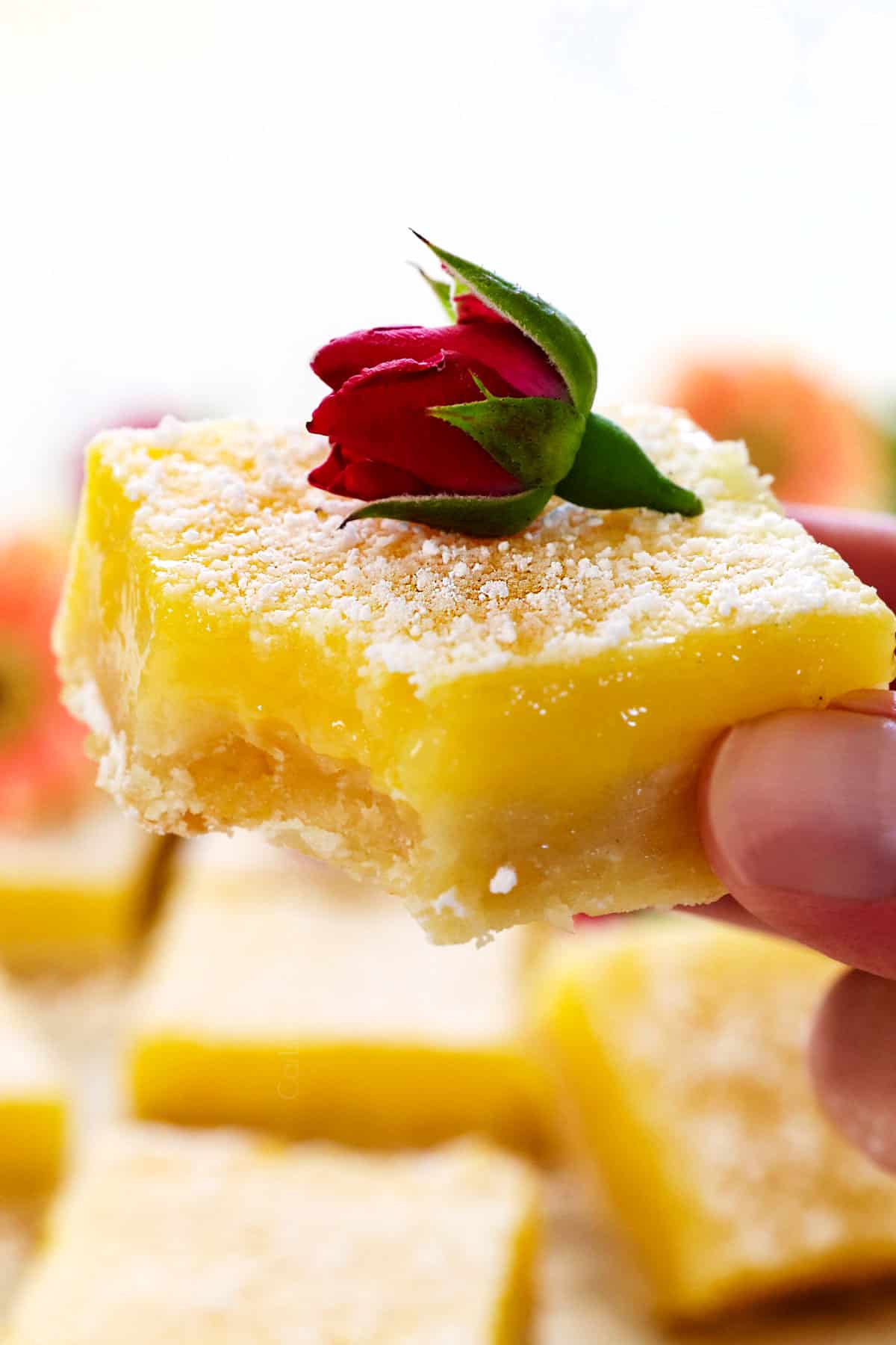 holding a lemon bars recipe with a bite taken out of the bar showing how soft it is