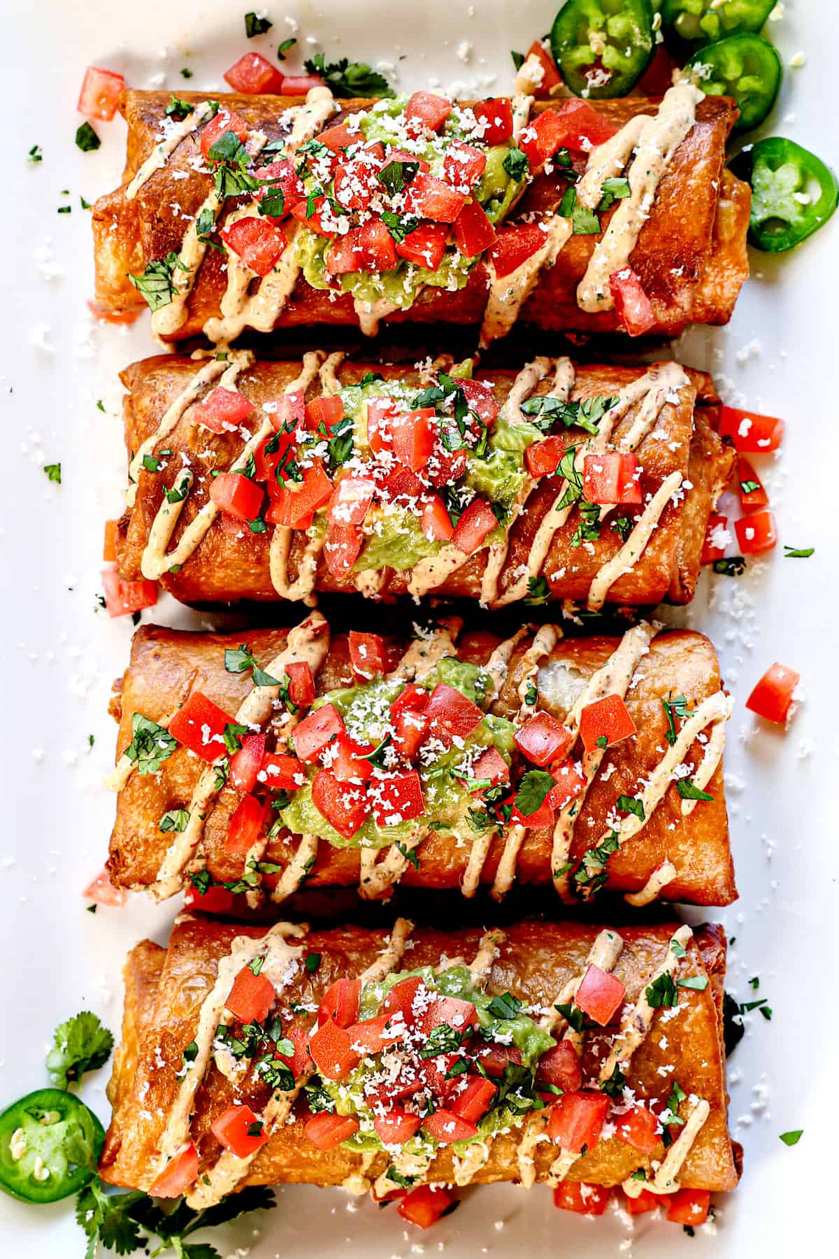 top view of chimichangas on a plate garnished with tomatoes, cilantro, guacamole