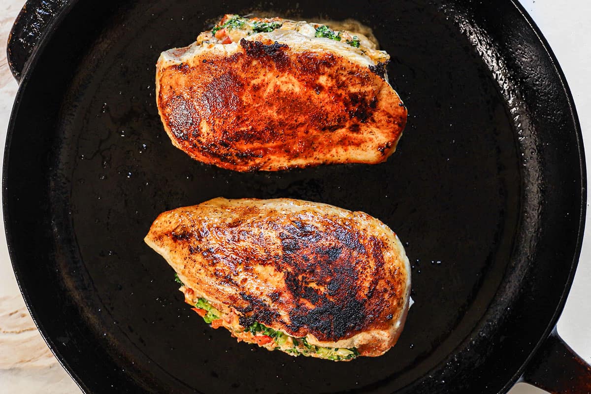 showing how to make stuffed chicken breast recipe by searing the chicken breasts in a cast iron skillet