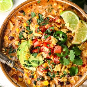 top view of serving slow cooker chicken taco soup in a bowl topped with tomatoes, cilantro, avocados, and limes
