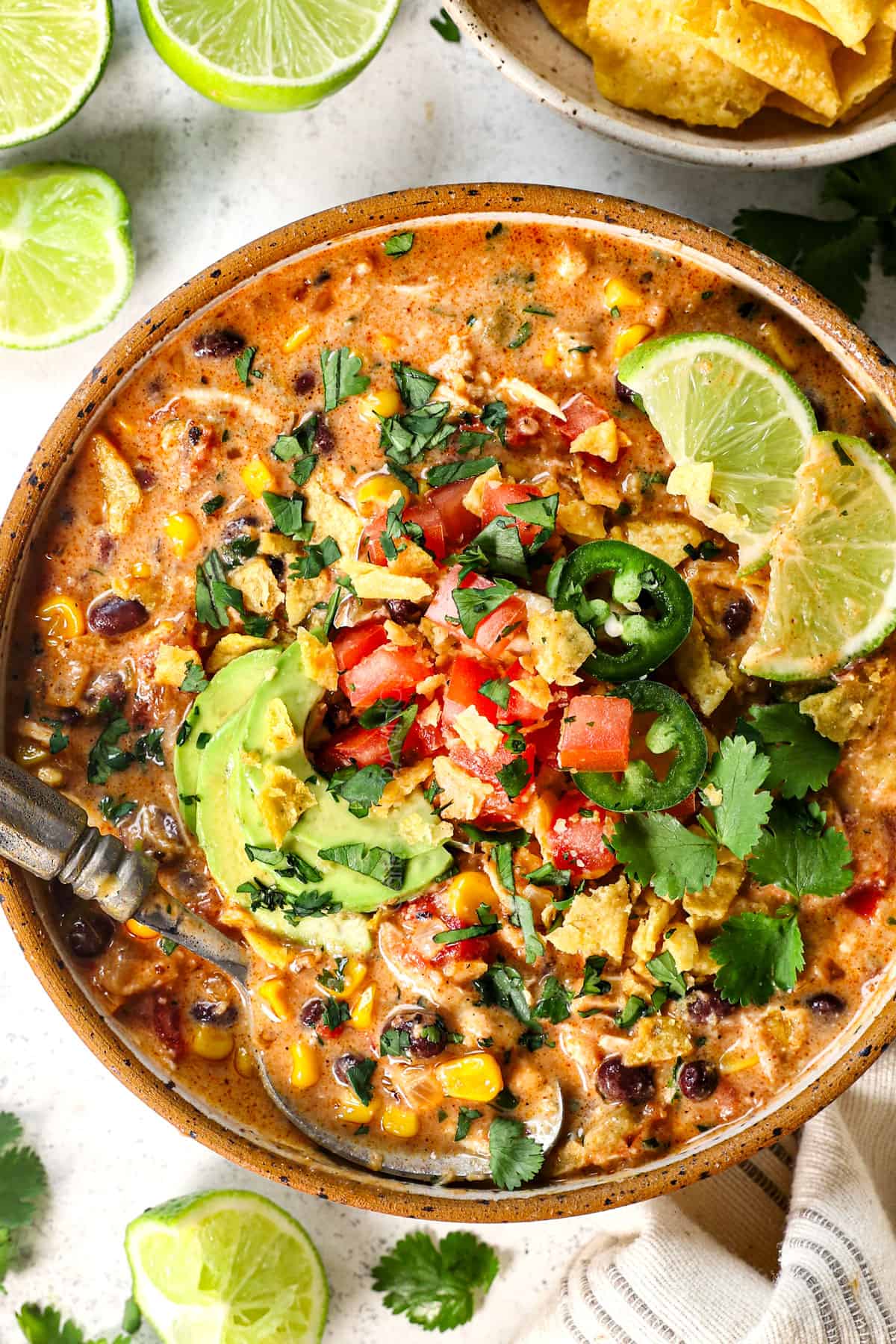 top view of serving slow cooker chicken taco soup in a bowl topped with tomatoes, cilantro, avocados, and limes