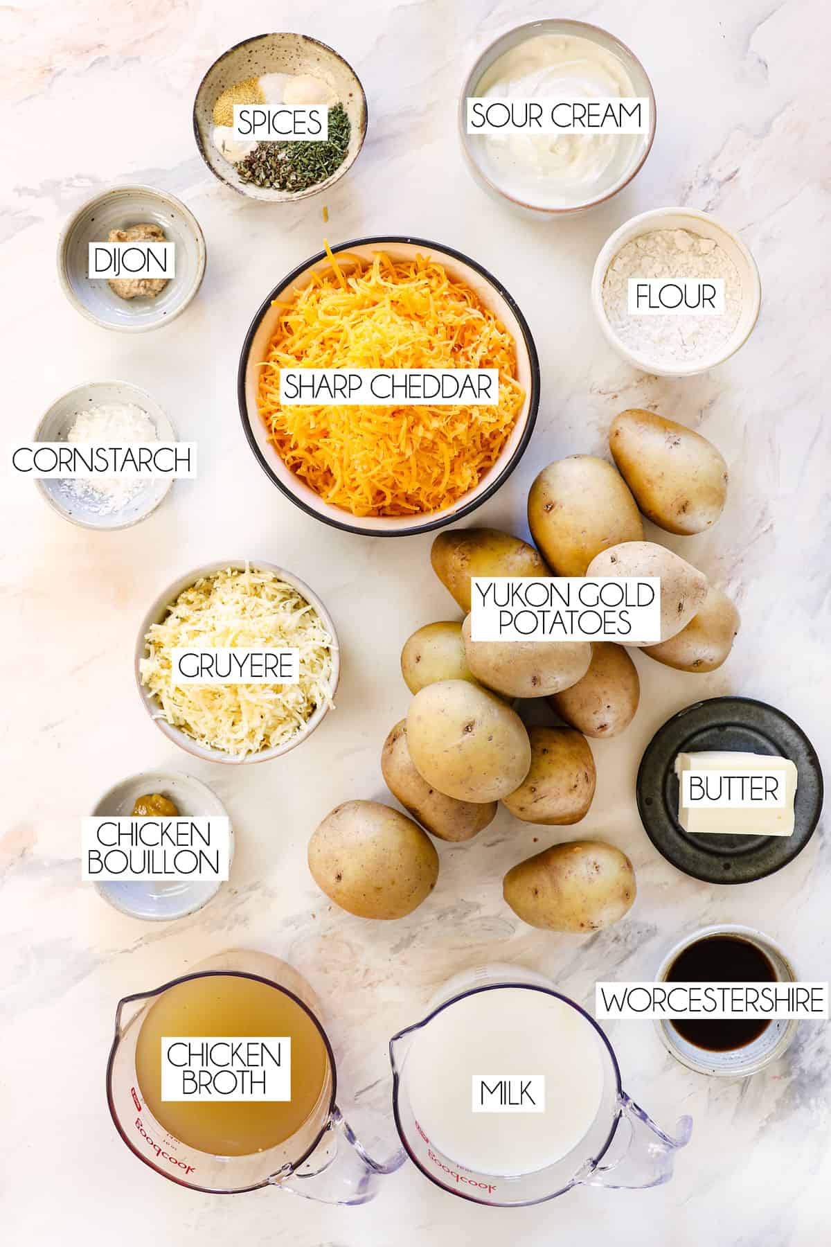 top view showing cheesy potato ingredients: Yukon gold potatoes, cheddar, Gruyere, butter, chicken broth, milk, butter, flour, spices