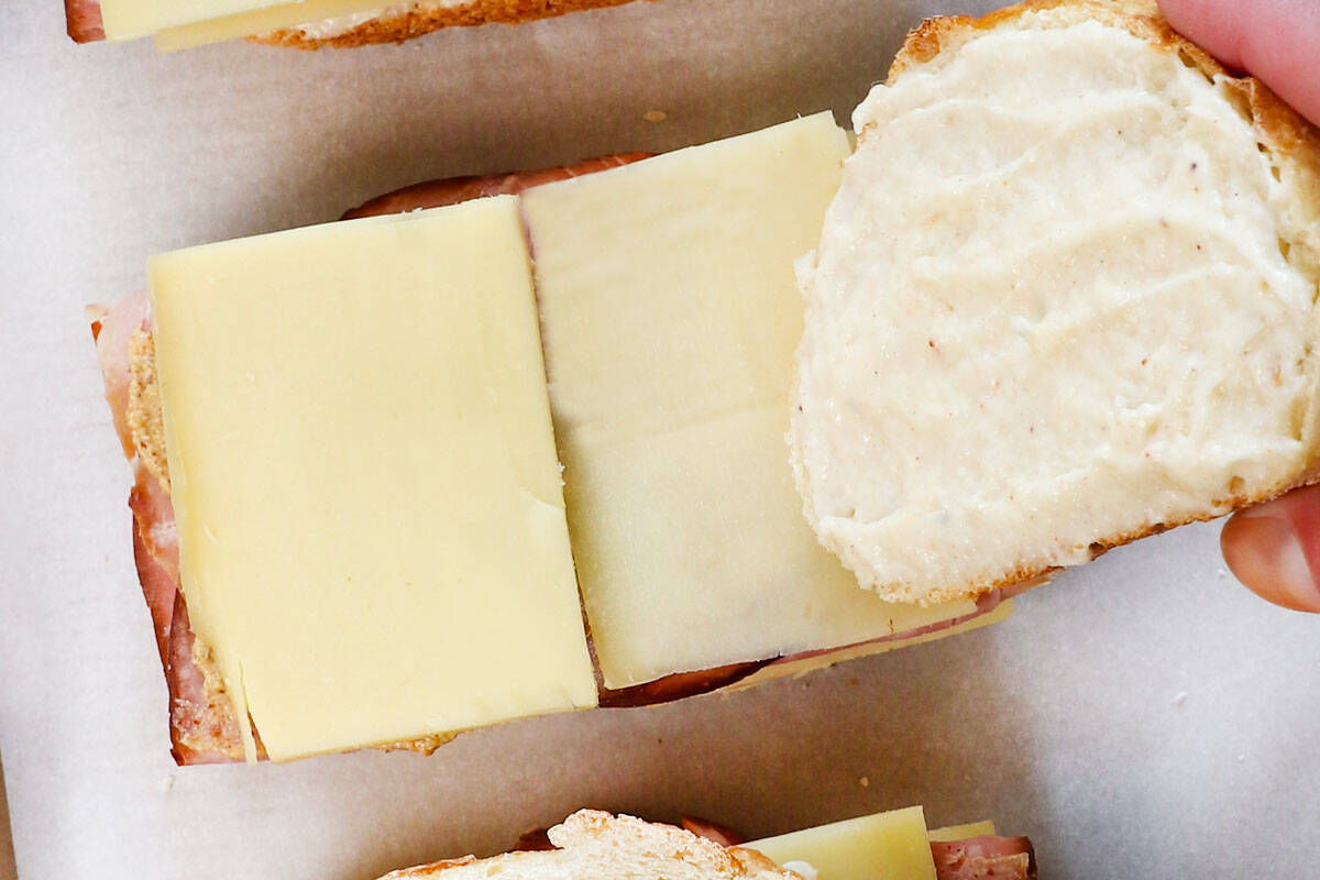 showing how to make croque monsieur by topping the sandwich a piece of bread, bรฉchamel side down