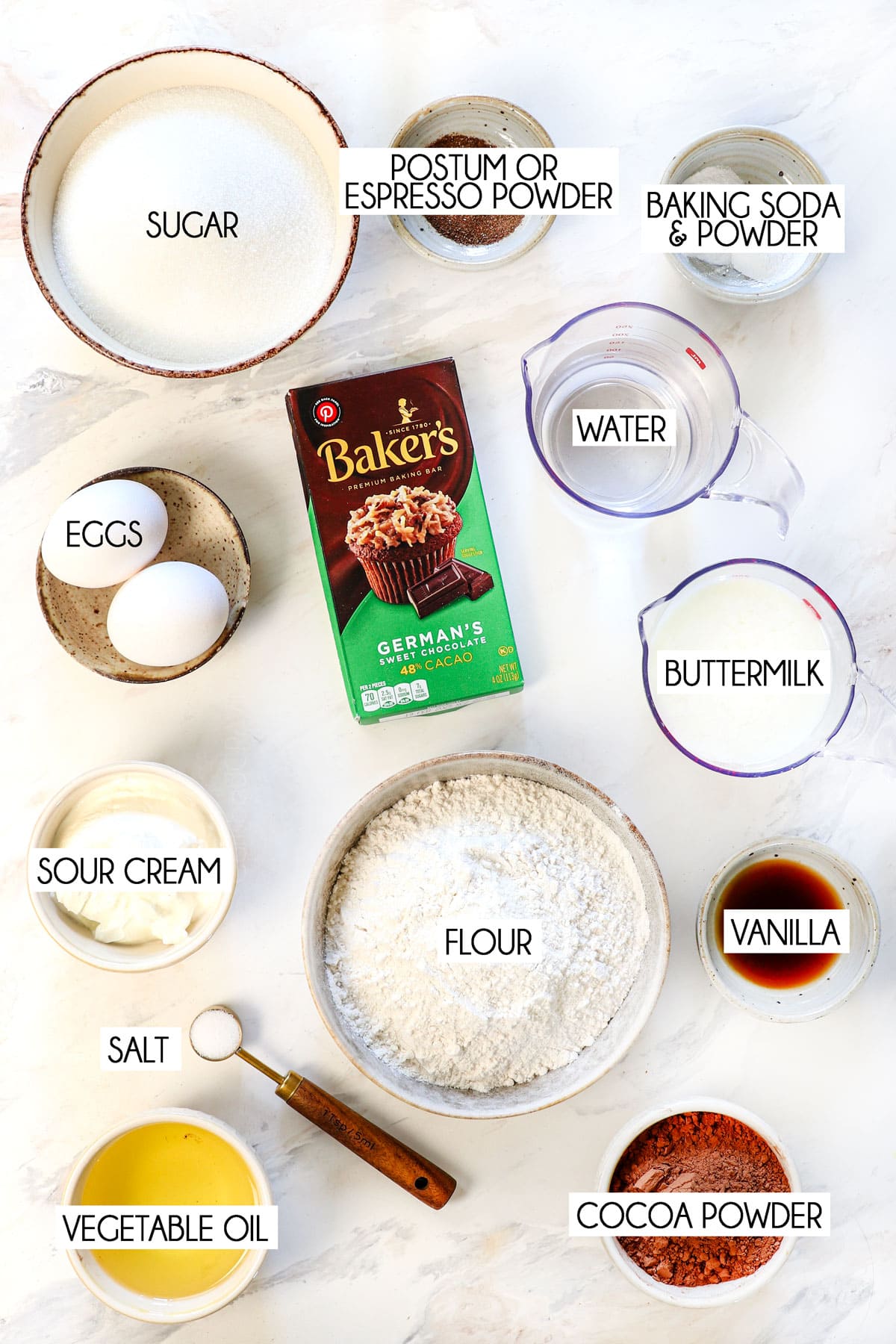 Top view of German Chocolate Cake Ingredients: Bakerโs German sweet chocolate (finely chopped), hot water, all-purpose flour, dark unsweetened cocoa powder, baking soda, baking powder, espresso powder (optional but recommended for extra depth), granulated sugar, salt, buttermilk at room temperature, full-fat sour cream at room temperature, vegetable oil, eggs at room temperature, and pure vanilla extract.