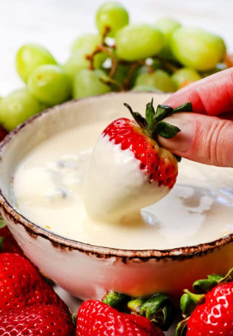 up close of dipping a strawberry in fruit dip with cream cheese showing how creamy it is