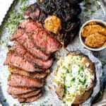 showing how to serve tomahawk steaks on a serving platter with baked potatoes, compound butter and fresh herbs