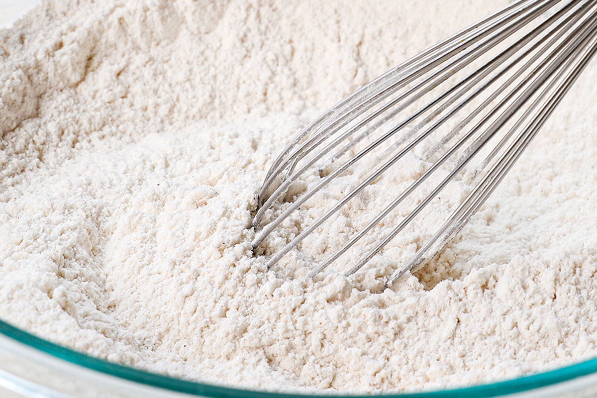 showing how to make fluffy pancakes recipe by whiskingย the flour, sugar, baking powder, cinnamon, and salt in a large mixing bowl.