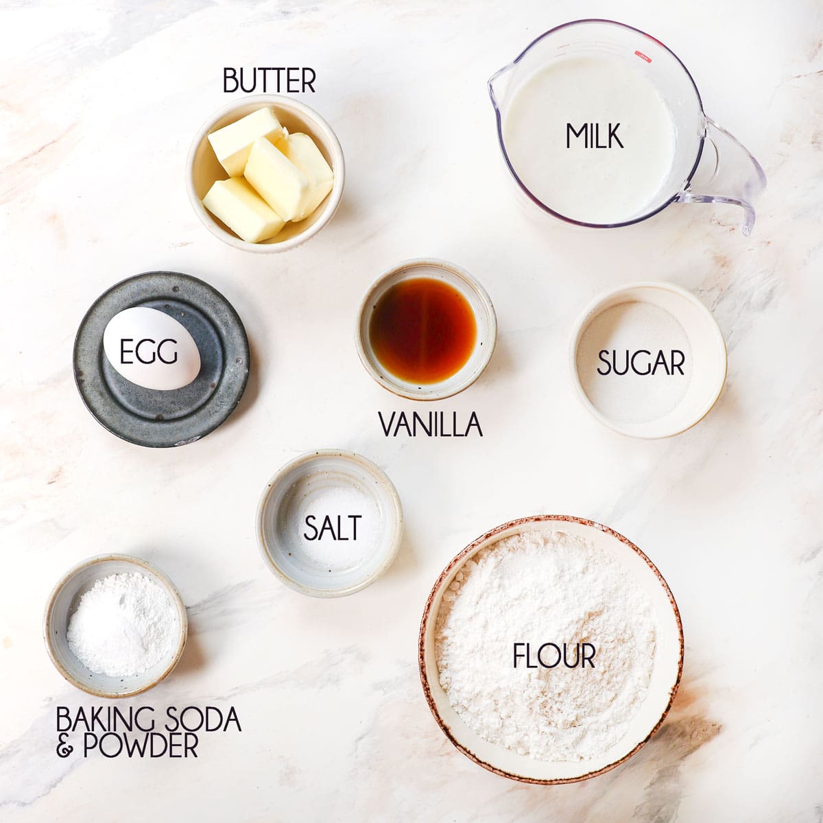 top view of pancake ingredients: flour, milk, egg, butter, baking powder, baking soda, salt, vanilla