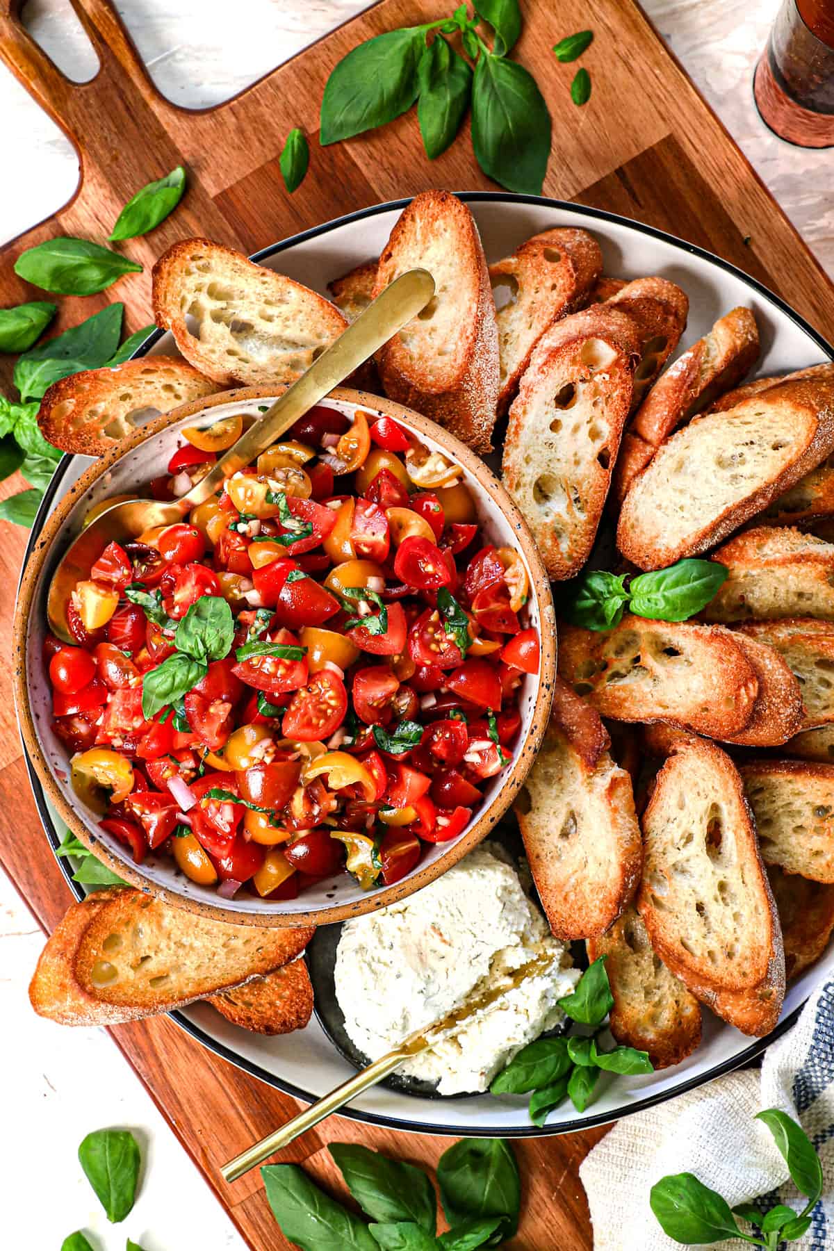 showing how to make bruschetta by adding the tomato bruschetta to a bowl on a platter and surrounding it with toast
