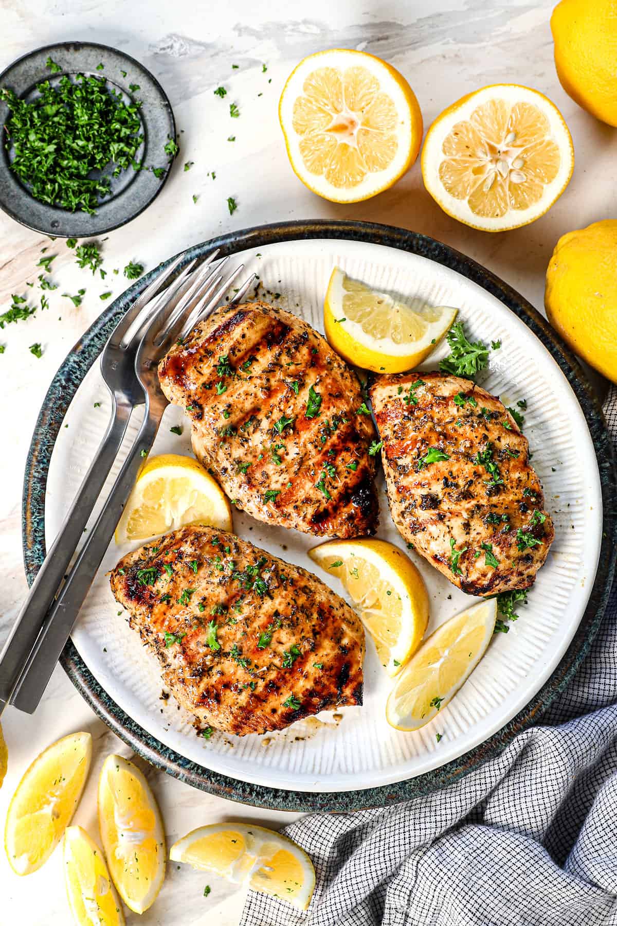 top view of grilled chicken recipe on a plate served with fresh lemons and parsley