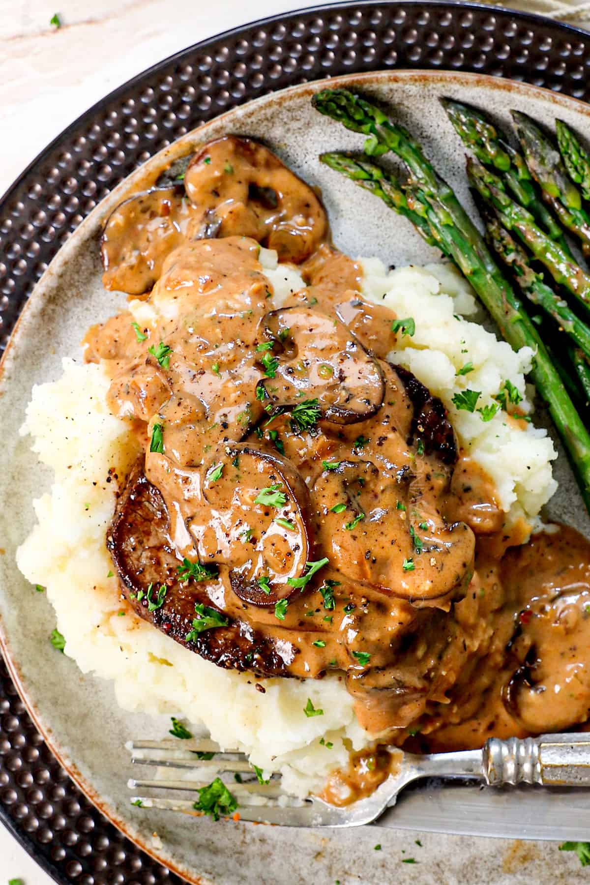 showing how to serve Steak Diane recipe on a plate with mashed potatoes and asparagus, garnished by fresh parsley