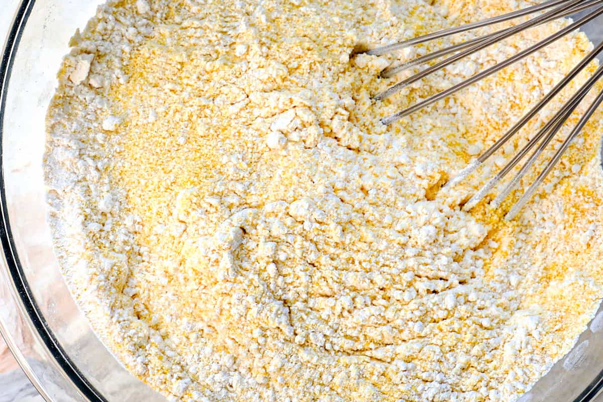 showing how to make cornbread by whisking together the cornmeal, flour, baking soda, baking powder and salt in a bowl