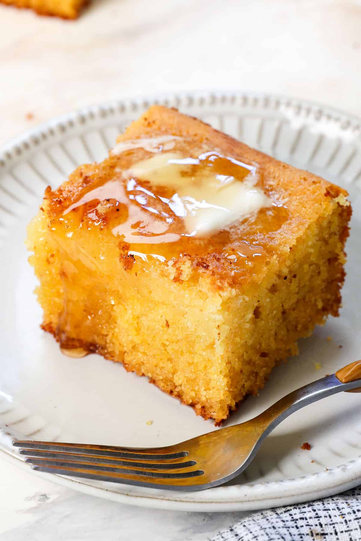 up close of a slice of best cornbread recipe on a plate with butter and honey on top