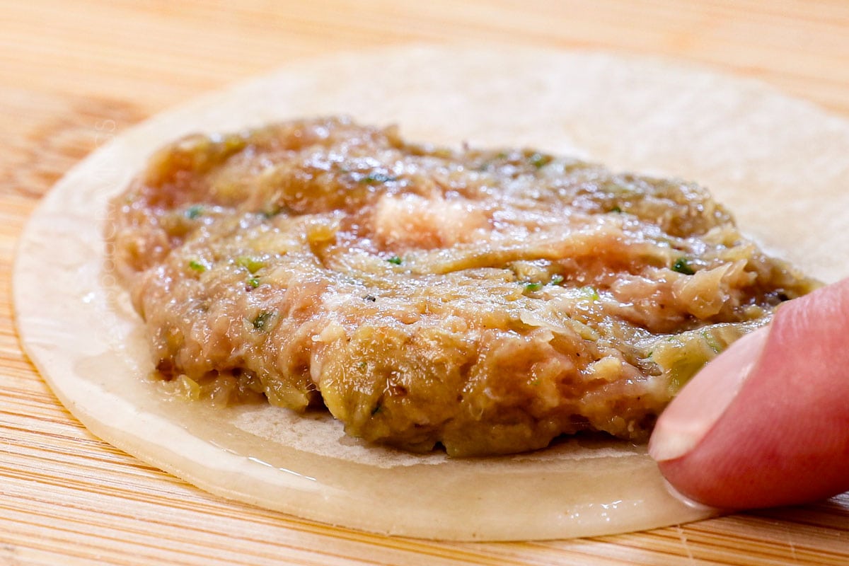 showing how to make gyoza dumplings by adding the filling to a gyoza wrapper, flattening it into a half circle, then running water around half of the wrapper with a finger