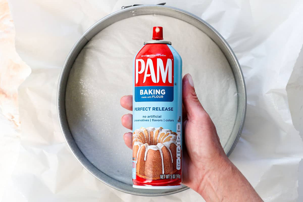 showing how to make no bake cheesecake by lining a springform pan with parchment paper and spraying with nonstick cooking spray