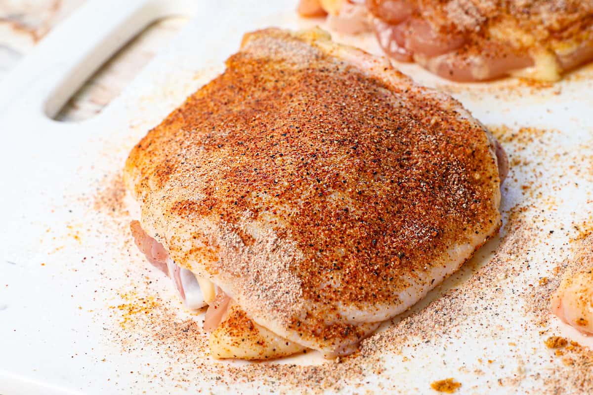 showing how to cook chicken thighs in air fryer by adding the spice rub to the chicken