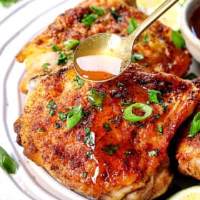 chicken thighs in air fryer with a glaze being drizzled on