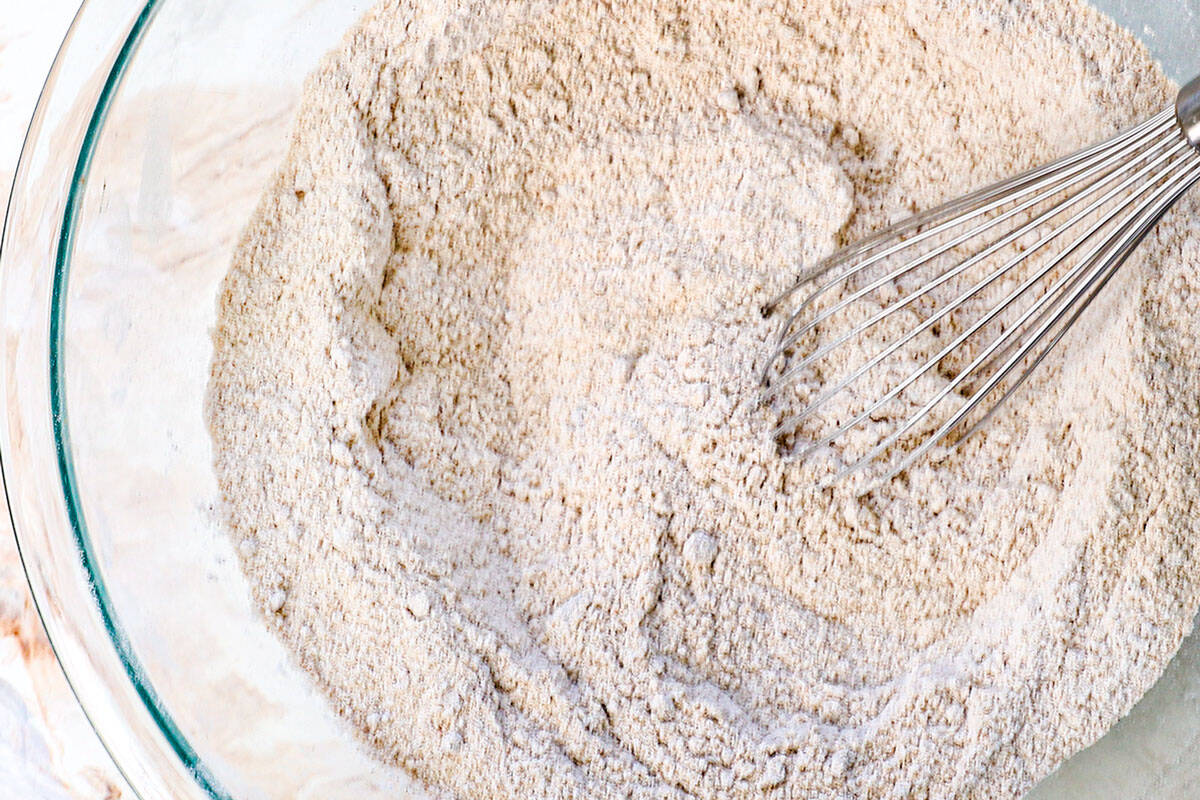 showing how to make zucchini bread by whisking the flour, baking soda, baking powder, ground cinnamon, ground nutmeg, salt and cardamom