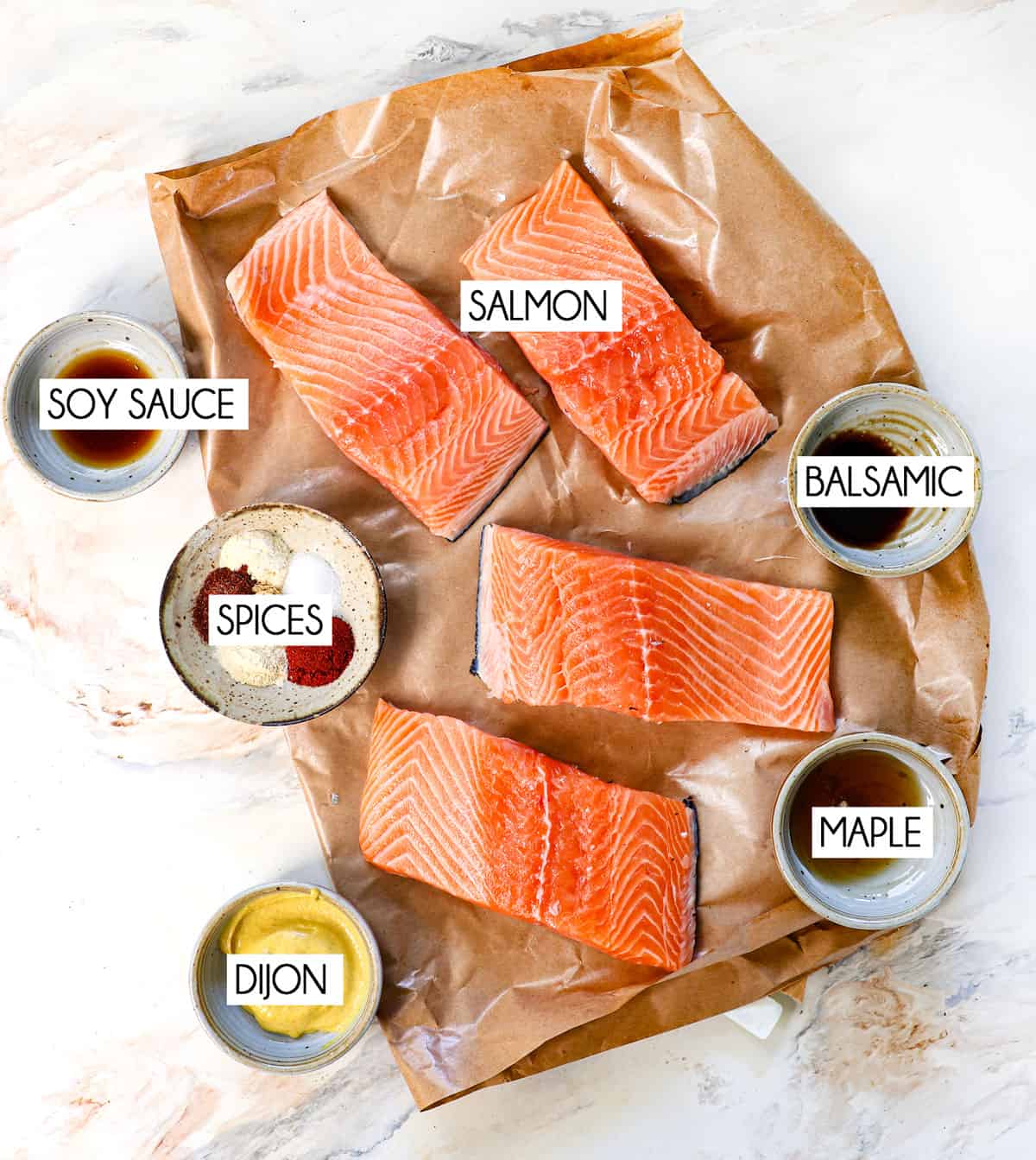 top view of air fryer salmon ingredients: salmon filets, olive oil, Dijon mustard, soy sauce, balsamic vinegar, maple syrup, and spices