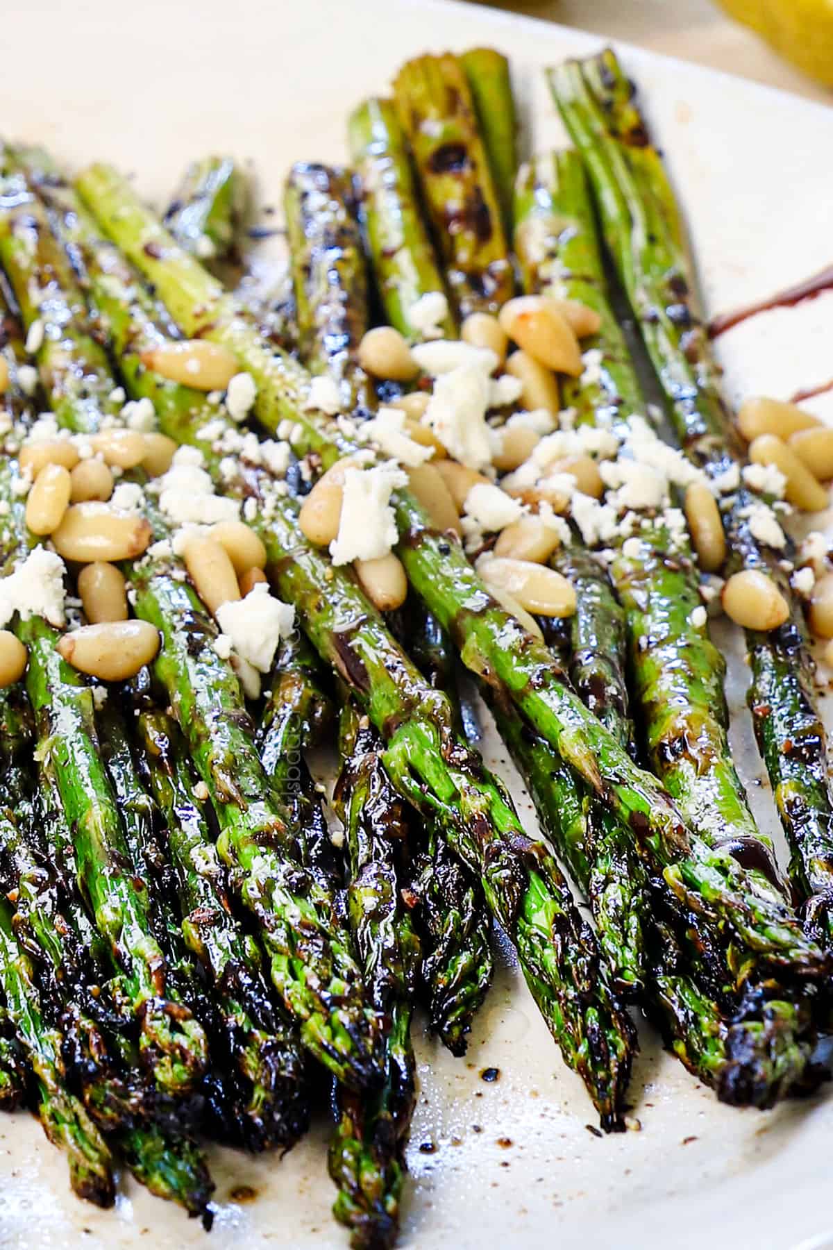 asparagus on the grill being served on a platter garnished with lemon and nuts