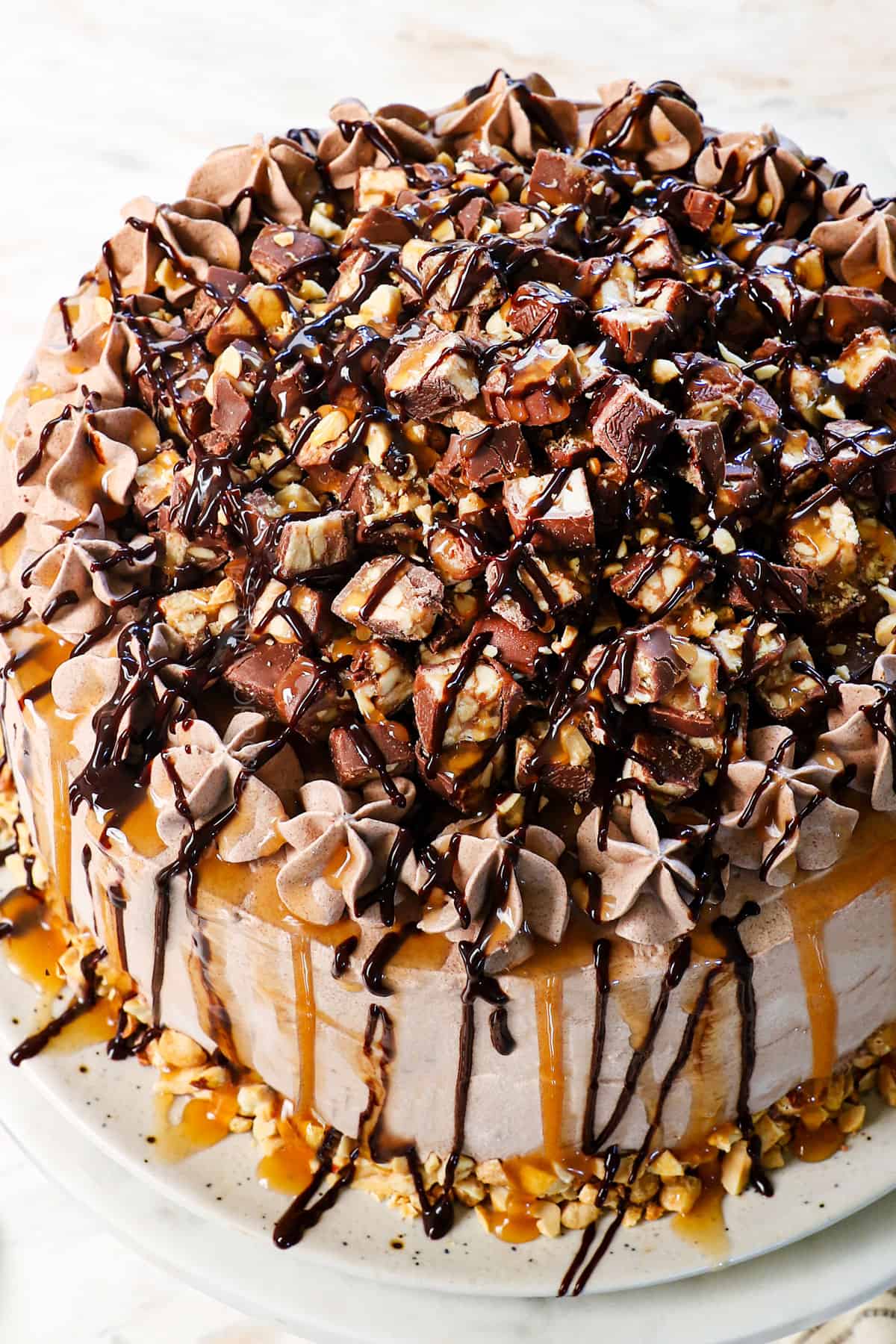 showing how to decorate diy ice cream cake with chopped candy bars, caramel and fudge sauce