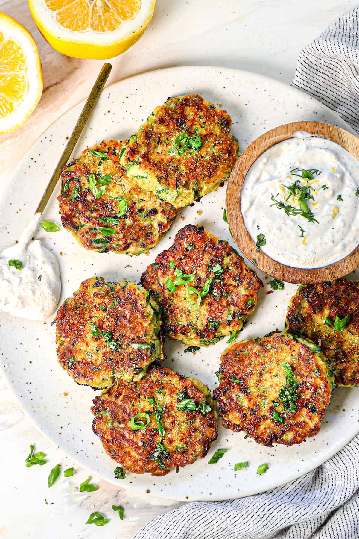 showing how to serve zucchini fritters on a plate garnished with green onions and served with garlic yogurt sauce