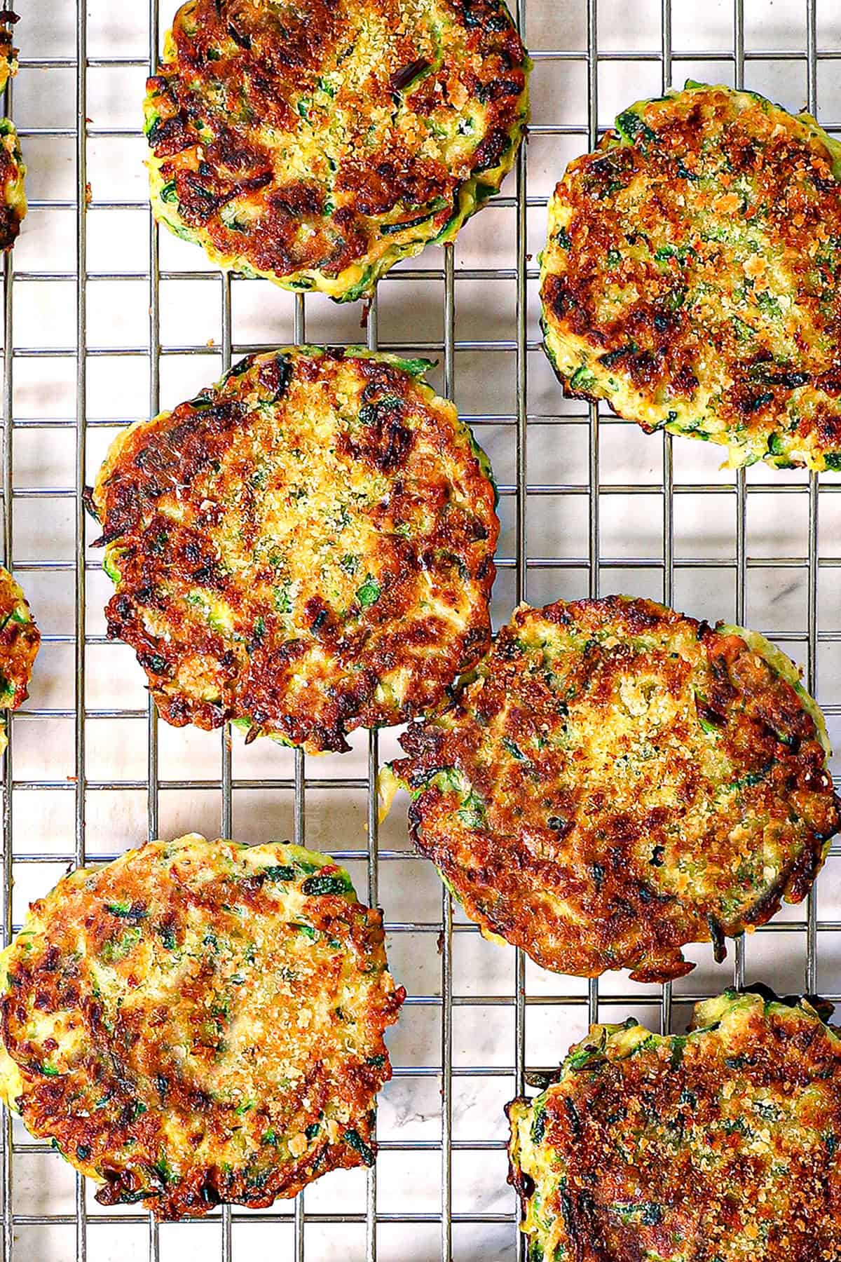 showing how to make zucchini fritters recipe by transferring the cooked fritters to a cooling rack